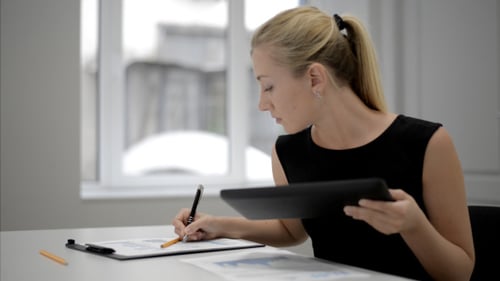 Woman Using Tablet and Writing in Office