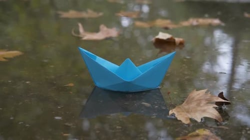 Blue Paper Boat Floating in Autumn Puddle