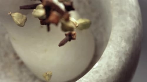 Mortero de granito y especies de especias de cardamomo y clavo cayendo en cámara lenta
