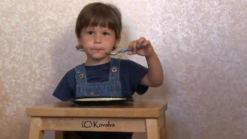 Adorable Child Eating with Spoon at Table