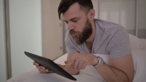 Man Relaxing in Bed Using a Tablet