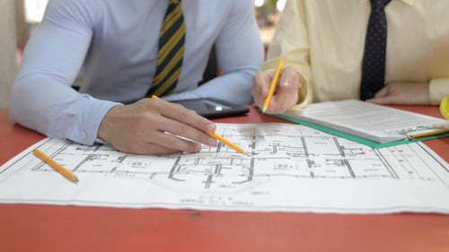 Two Men Reviewing Building Blueprint and Writing Notes