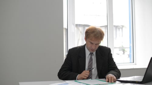 Man Signing Documents at Desk in Bright Office