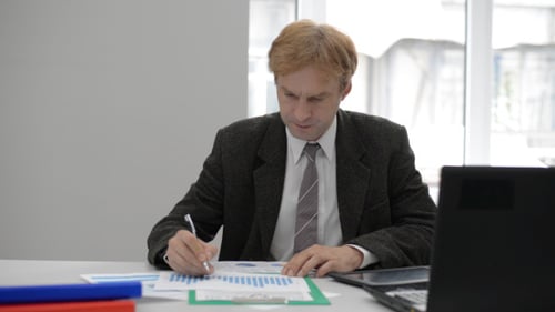 Focused Man Analyzing Data and Graphs at Office Desk