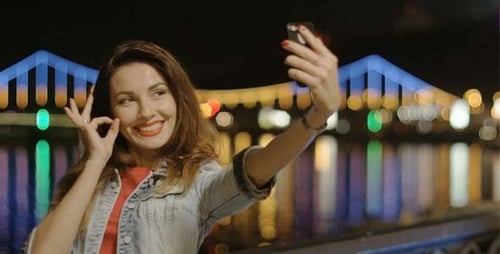 Woman Taking Vibrant Nighttime Selfies by Colorful Bridge