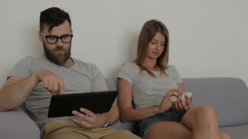 Couple Using Phone and Tablet on a Couch