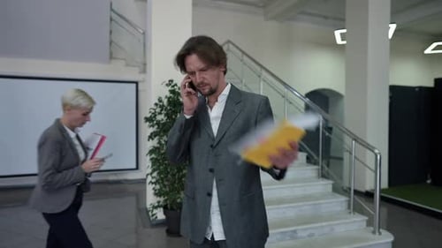 Stressed Troubled Caucasian Man Talking on Phone Shaking Paperwork Walking in Office Lobby with