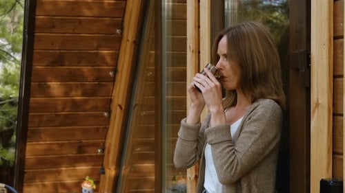 Woman Relaxing Outside Rustic Wood Cabin With Coffee