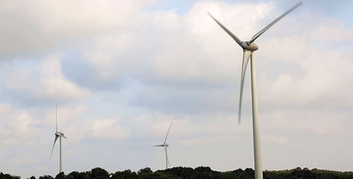 Three Tall Wind Turbines Turning Against Cloudy Sky