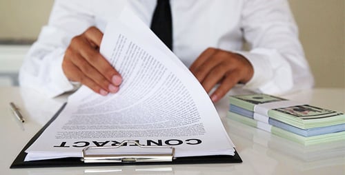 Adult Signing Contract Next to Stack of Money