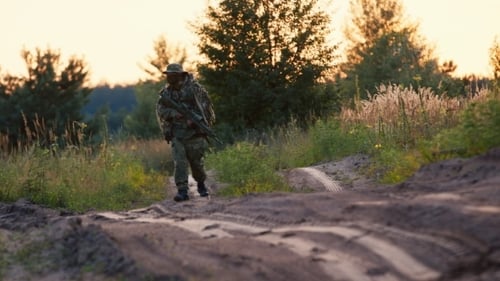 Camouflaged Person Walking with Rifle at Sunset