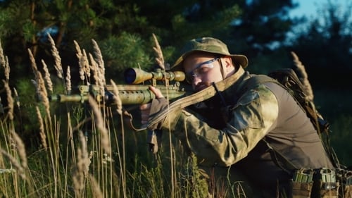 Man Aiming Rifle Kneeling in Tall Grass