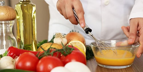Person Whisking Eggs with Fresh Vegetables Nearby