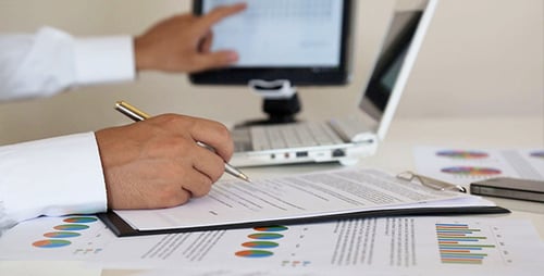 Person Working on Charts and Laptop at Desk