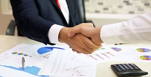 Business Handshake Over Charts in Office Setting
