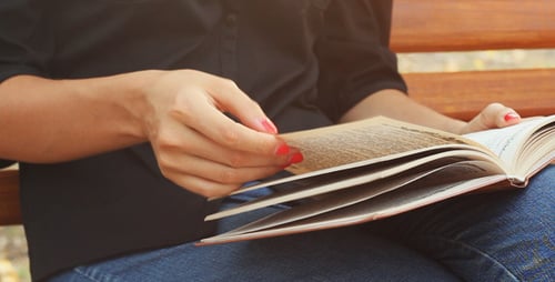 Girl Sits on a Bench in the Park and Reading Book