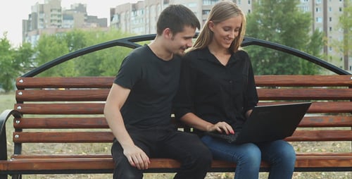 Friends Using Laptop on Park Bench
