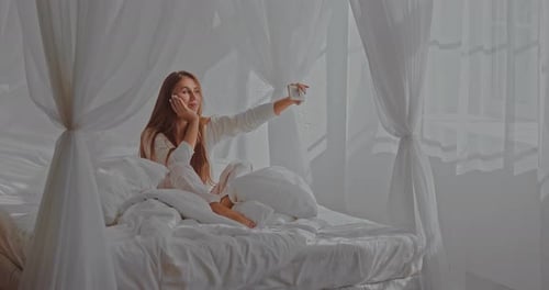 Attractive Woman Taking Selfies in Bright White Bed