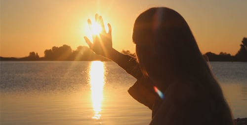 Woman Reaches Towards Setting Sun Over Water