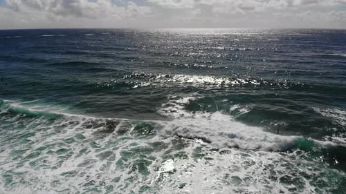 Luftaufnahme von tiefblauen Meereswellen, Sonnenreflexion und Wolken im Hintergrund