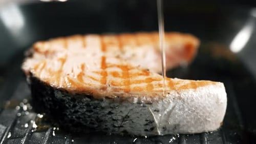A Salmon Fillets on a Grill Plate is Pouring with Olive Oil