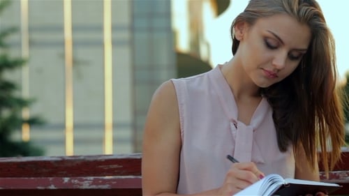 Focused Young Woman Writing in Notebook Outdoors