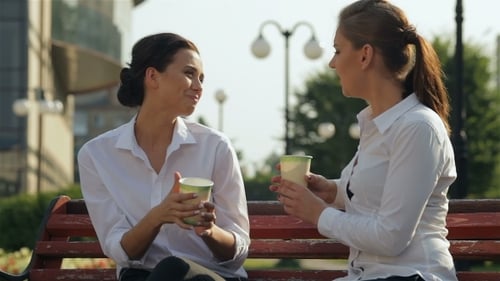 Two Women Laughing and Talking on Bench in Park