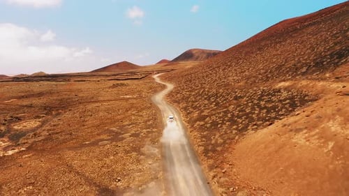 One White SUV Car Driving Alone Travel on Empty Dirt Road Freeway Through Desert Volcanic Landscape