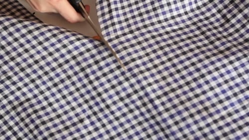 Hands Cutting Checkered Fabric with Scissors Close Up