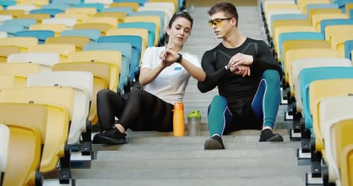 Couple Looking at Smart Watches in Stadium Seating