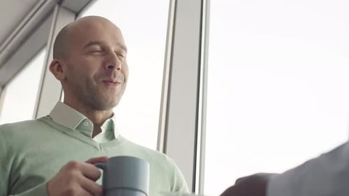 Smiling Man Holding Coffee Cup in Bright Office