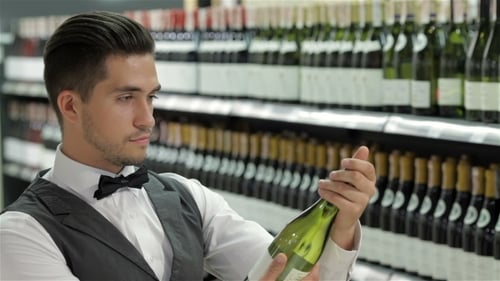 Man Selects White Wine Bottle in Supermarket Aisle