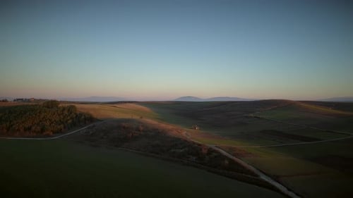 Aerial view of beautiful hills with lots of grass and trees at sunset.