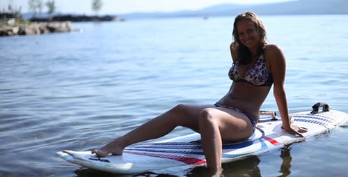 Woman Smiling, Sitting on Surfboard in Lake