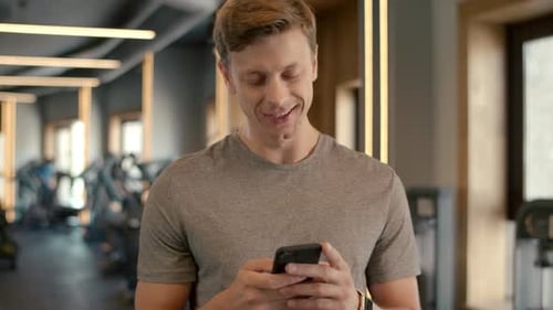 Cheerful Bodybuilder Standing at Gym. Sportsman Texting Message in Sport Club