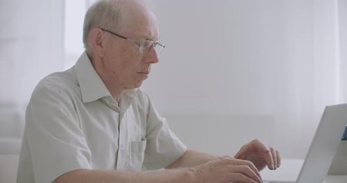 Senior Man Typing on Laptop Computer at Home