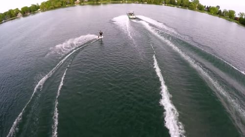 Drohnenaufnahme aus der Vogelperspektive eines Mannes beim Wakeboarden hinter einem Boot.