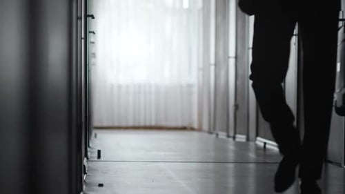 Man Silhouette Walking Away with Suitcase Down Hall