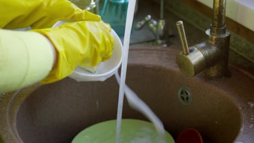 Housewife in Yellow Gloves Washes Plate in the Sink with a Sponge and Detergent