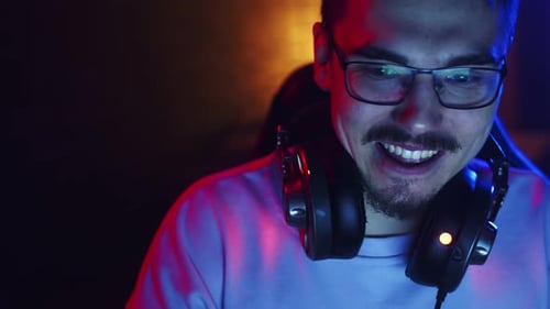 Young man with headphones is playing computer games, rejoicing and clapping hands, front view.