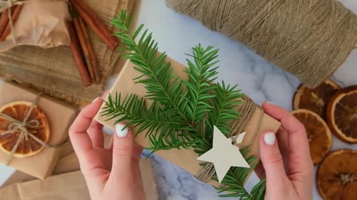 Woman Making Box with New Year's Gifts Wrapped in Craft Paper and Decorated with Fir Branch