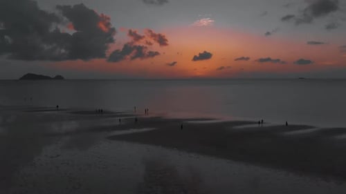 Aerial flight above people walking on the beach against coloful sunset