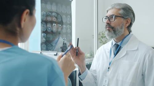 Radiologist Talking to Assistant Dicsussing Brain Images Looking at MRI Scans in Clinic