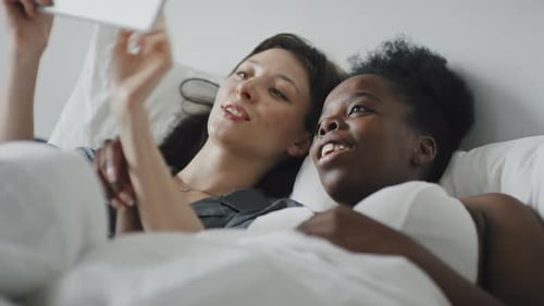 Happy Female Couple with Tablet Relaxing in Bed