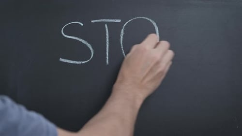 Hand Writes 'Stop Racism' on Blackboard with Chalk