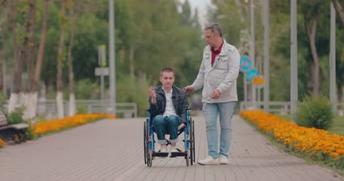 Man Helping Young Adult in Wheelchair Through Park