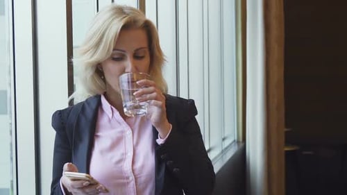 Businesswoman Using Phone and Drinking Water in Office