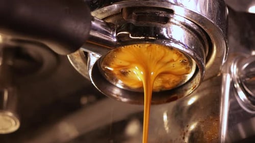 Closeup of pouring coffee stream from professional machine through the bottomless portafilter type