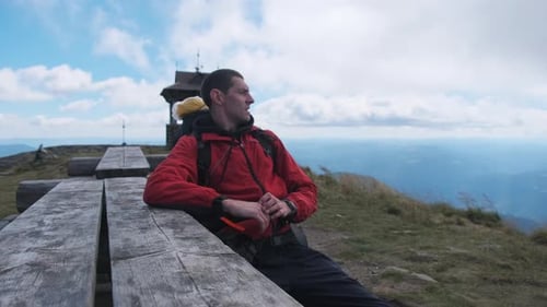Tourist with Backpack on Top of Mountain Sat Down To Rest at an Old Wooden Table