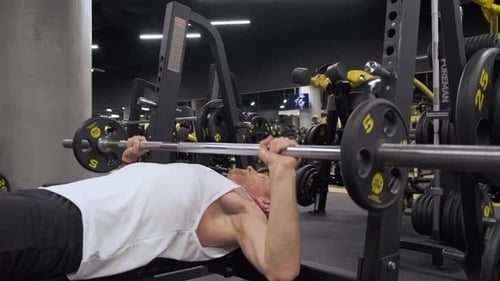 A young European Man is Lying On a Bench Doing an Exercise Lifting a Barbell in the Gym